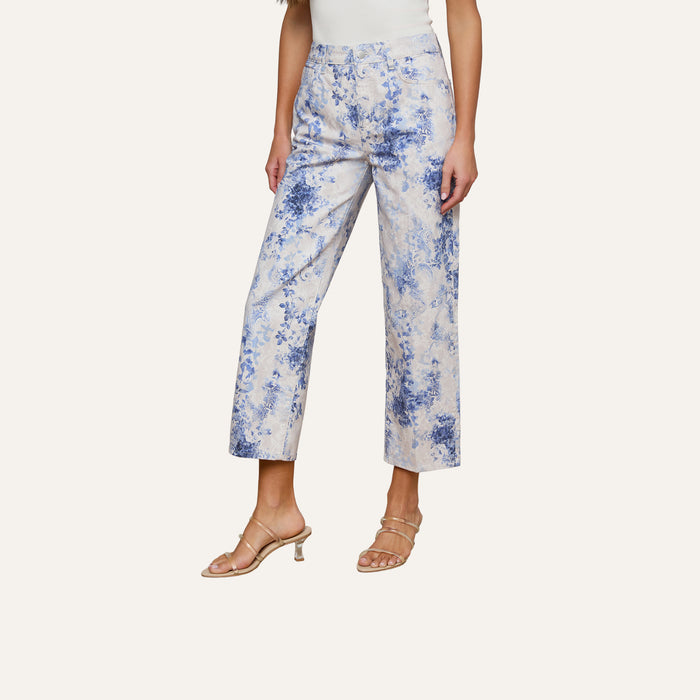 A woman wears the June Cropped Stovepipe Jean featuring a blue floral paisley print, paired with a white top and nude heeled sandals, standing against a plain light background.