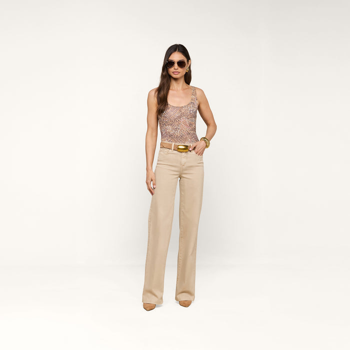 Woman wearing sunglasses, the Kalea Mesh Bodysuit, beige high-waisted pants, a belt, and heels stands against a plain white background.