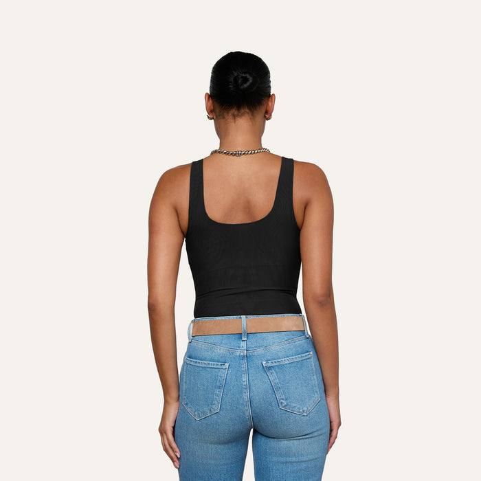 A person with hair in a bun, wearing the Kalea Mesh Bodysuit, blue jeans, and a chain necklace, is seen from the back against a plain light background.