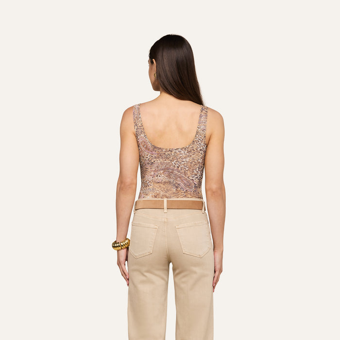 A woman with long brown hair is shown from behind, wearing the Kalea Mesh Bodysuit—a sleeveless leopard paisley print top—along with beige pants and bracelets on her left wrist, standing against a plain light background.
