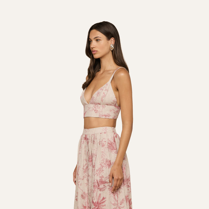 A woman with long brown hair wears the Kaori Linen Bralette Top in pink and cream floral, paired with a high-waisted skirt. She is standing sideways against a plain white background.