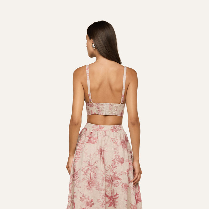 A woman with long brown hair, wearing the sleeveless Kaori Linen Bralette Top in a jungle toile print and a matching high-waisted skirt, stands facing away with her hands at her sides against a plain light background.