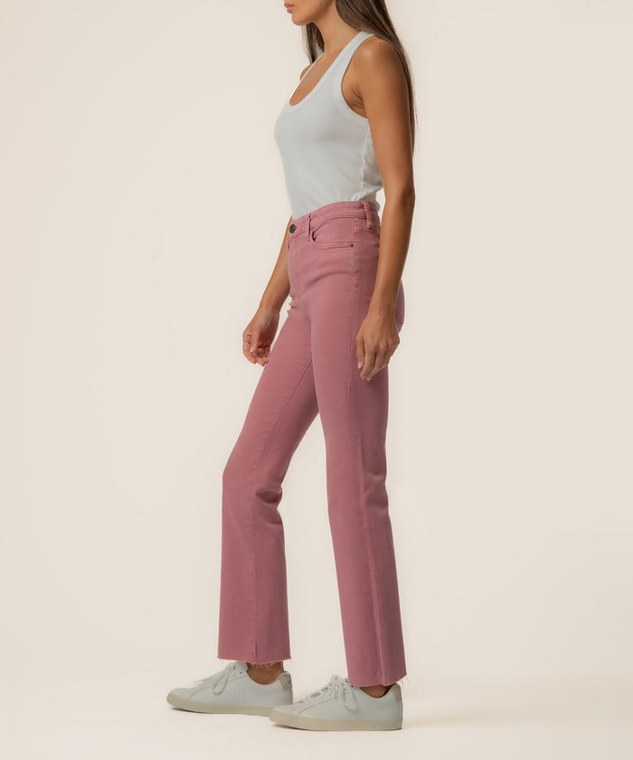 Woman wearing rose pink high-rise ankle flare jeans with white tank top and white sneakers, shown from the side.