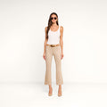 A woman stands against a plain white background, facing forward with her hands relaxed by her sides, wearing sunglasses, a white tank top, beige heels, and the Kendra Coated Cropped Flare Jean in high-rise beige.
