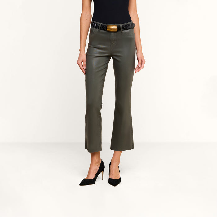 A person wearing the Kendra Coated Cropped Flare Jean in ash olive green, paired with a black top, black high heels, and a black belt featuring a large rectangular buckle, stands against a plain white background.
