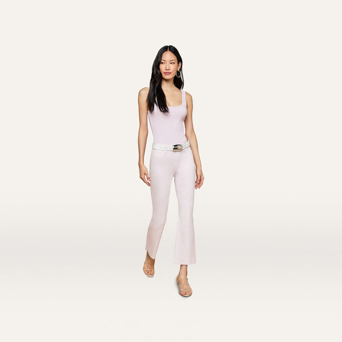 A woman with long black hair wears a light purple tank top, a white belt, beige heeled sandals, and the Kendra Coated Cropped Flare Jean, standing against a plain white background.