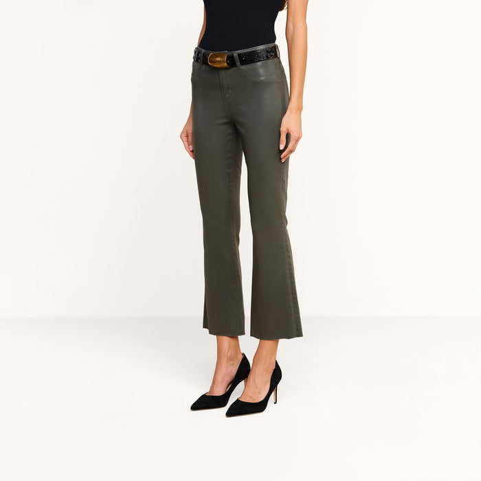A person wearing the Kendra Coated Cropped Flare Jean in ash olive green, paired with a black sleeveless top, a black belt, and black high heels stands against a plain white background.