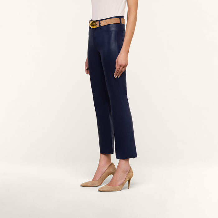 A person stands against a white background wearing the Kendra Coated Cropped Flare Jean, a tan belt, a white top, and beige heels. Only the lower half of their body is visible.