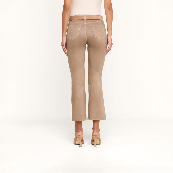 A woman wearing the Kendra Coated Cropped Flare Jean stands with her back to the camera against a plain white background, paired with beige heels.