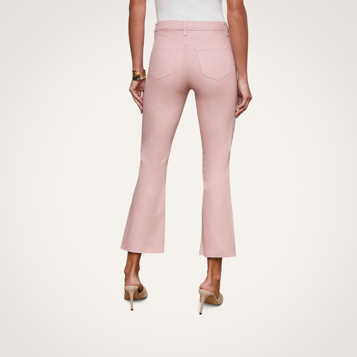 A woman is shown from the back against a plain white background wearing the Kendra Coated Cropped Flare Jean in light pink, paired with a white top and beige heels.