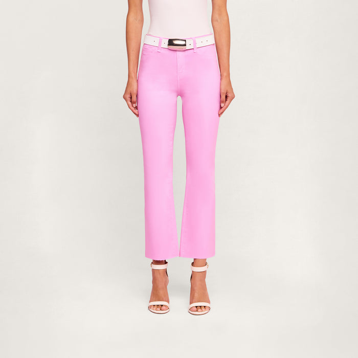 Wearing the Kendra Coated Cropped Flare Jean in bright pink coated denim, styled with a white belt and white high-heeled sandals, a person stands against a plain light background.