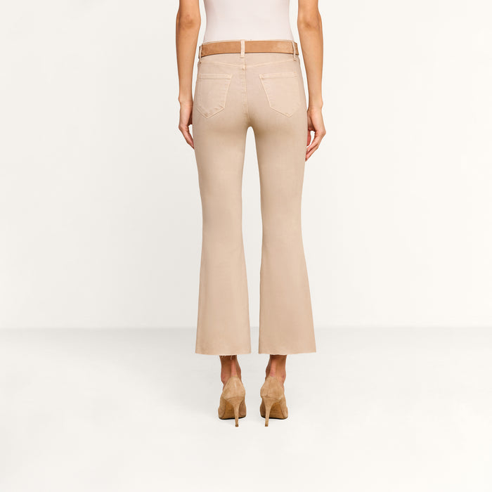A person wearing the Kendra Coated Cropped Flare Jean and tan high heels stands facing away in a plain, light-colored room.