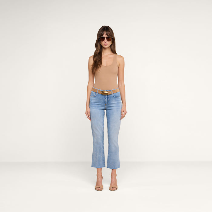 A woman wearing sunglasses, a tan sleeveless top, the Kendra Cropped Flare Jean in light wash, a brown belt, and beige heels stands facing forward against a plain white background.