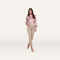 A woman stands against a white background wearing a silky pink blouse, the Kendra Cropped Flare Jean in neutral tan super stretch denim, and beige heeled sandals, with one hand in her pocket.
