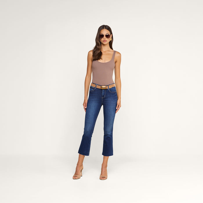 A woman wearing sunglasses, a sleeveless taupe bodysuit, heeled sandals, and the Kendra Cropped Flare Jean stands against a plain white background.