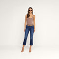 A woman wearing sunglasses, a sleeveless taupe bodysuit, heeled sandals, and the Kendra Cropped Flare Jean stands against a plain white background.
