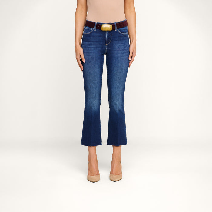 A person wearing the Kendra Cropped Flare Jean in blue, styled with a beige top, a burgundy belt, and beige heels stands facing forward against a plain white background.