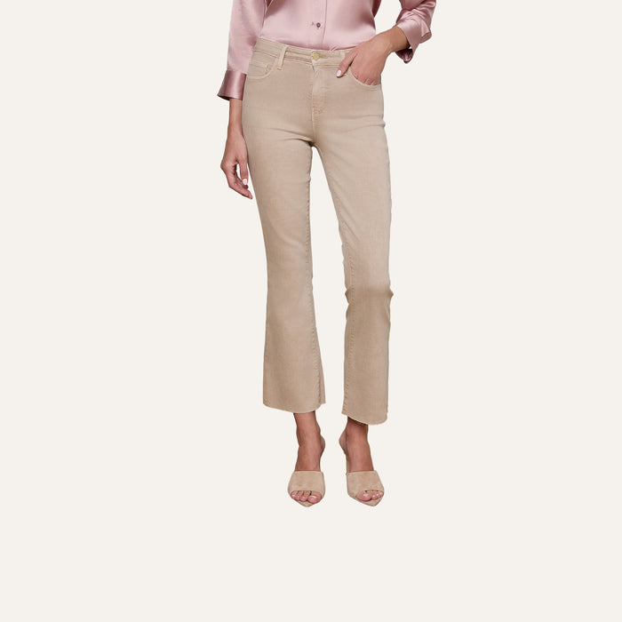 A person wearing the Kendra Cropped Flare Jean in neutral tan, paired with a light pink satin blouse and beige heeled sandals, stands against a plain light background.