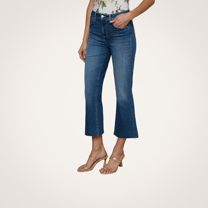A person models the Kendra Cropped Flare Jean in a dark denim wash, paired with a floral top and beige heeled sandals, posing against a plain white background with only the lower half of the body visible.