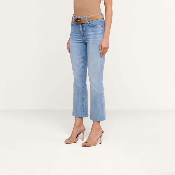A person wearing the Kendra Cropped Flare Jean, a tan sleeveless top, a brown belt, and beige high-heeled sandals stands against a plain white background. Their head and lower arms are not visible.