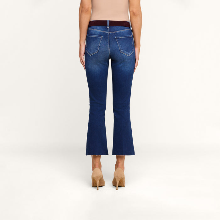 A person wearing Kendra Cropped Flare Jeans in high-rise blue super stretch denim and beige high-heeled shoes stands facing away against a plain white background.