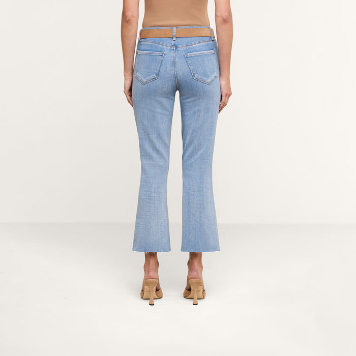 A person is shown from the back wearing the Kendra Cropped Flare Jean in a light wash, paired with a brown sleeveless top and beige heeled shoes, standing against a plain white background.