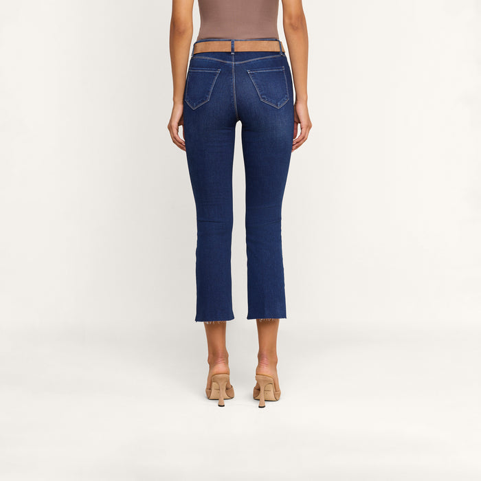 A person wearing high-heeled shoes and the Kendra Cropped Flare Jean, made from stretch denim with a sheer waistband and back pockets, is seen from behind against a plain white background.
