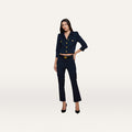 A woman stands against a plain background, wearing the Ketra Bootcut Trouser in midnight navy, paired with a matching tailored jacket featuring gold buttons and crafted from stretch suit fabric. She completes the look with black heels, standing with one hand on her hip and a neutral expression. The baby bootcut silhouette of the Ketra trousers adds a modern touch to her outfit.