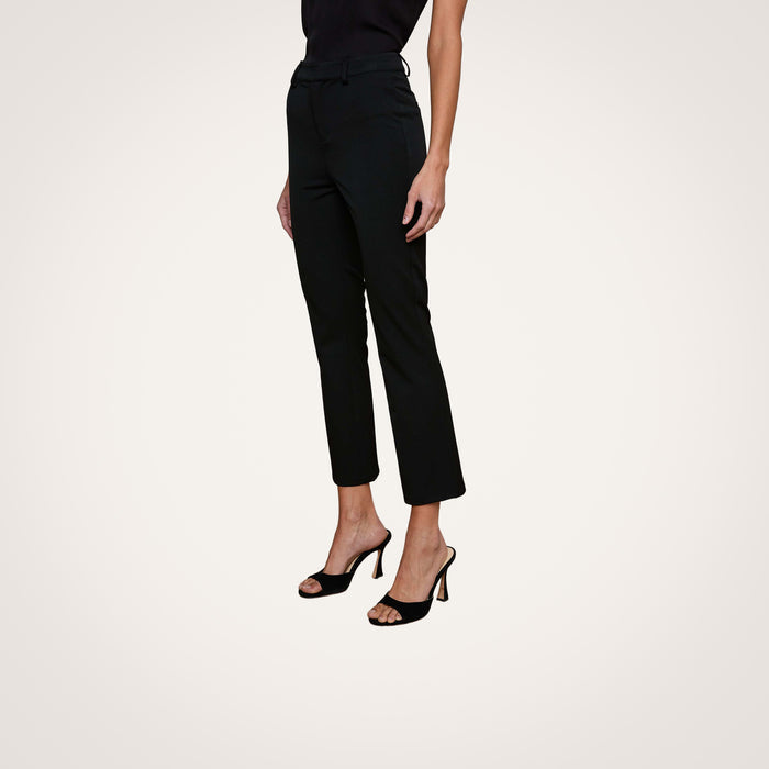 A woman is wearing the Ketra Bootcut Trouser in black, paired with a black sleeveless top and black high-heeled sandals, standing against a plain light background with her arms relaxed at her sides.