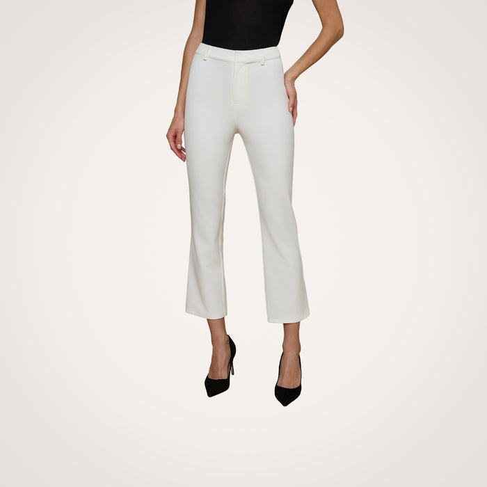 A woman is wearing the Ketra Bootcut Trouser in high-waisted white stretch suit fabric, styled with black heels and a black sleeveless top, standing against a plain light background. Only her body from the shoulders down is visible.