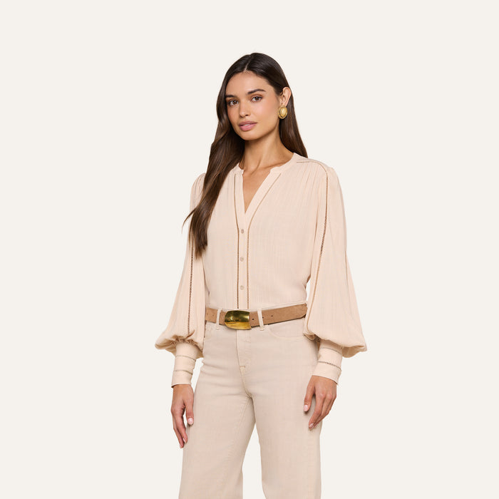 A woman wears the Kiera Blouse—a beige, textured rayon bohemian top with blouson sleeves—paired with beige pants, a brown belt, gold earrings, and her long dark hair styled loosely against a plain white background.