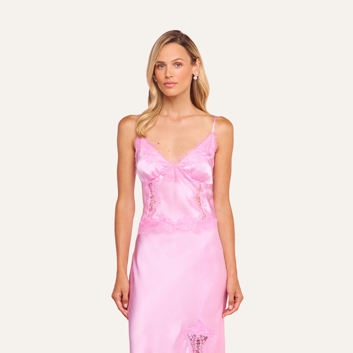 A woman with long blonde hair wears the Kimber Silk Lace Camisole and stands against a matching pink background, her expression neutral and arms by her sides.