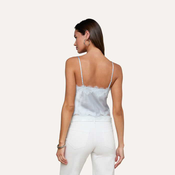 A woman with long brown hair is shown from the back against a plain light background, wearing the Kimber Silk Lace Camisole in light blue and white jeans.