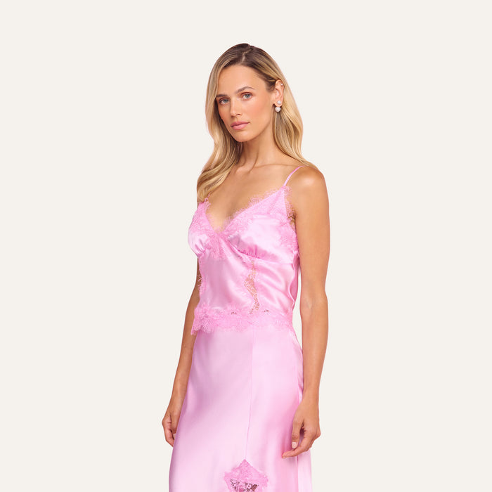 A woman with long blonde hair wears the Kimber Silk Lace Camisole, standing against a matching light pink background and looking at the camera with a neutral expression.