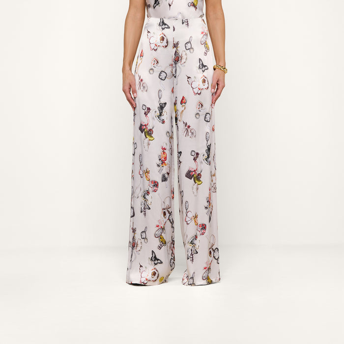 A person, shown from the lower torso down, stands against a plain white background wearing the Kimia Satin Pant—a high-rise, wide-leg style featuring a colorful butterfly print.