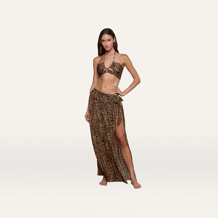 A woman poses barefoot against a plain white background, wearing a leopard print bikini top and the Klaire Cover-Up Skirt—a matching wrap skirt with a high slit crafted from lightweight viscose chiffon for an effortless look.
