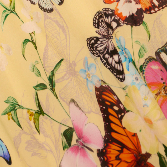 The Klaire Cover-Up Skirt showcases colorful butterflies and delicate flowers printed on light yellow viscose chiffon. The lively, spring-inspired pattern features vivid oranges, pinks, blues, and blacks with intricate floral and butterfly details.
