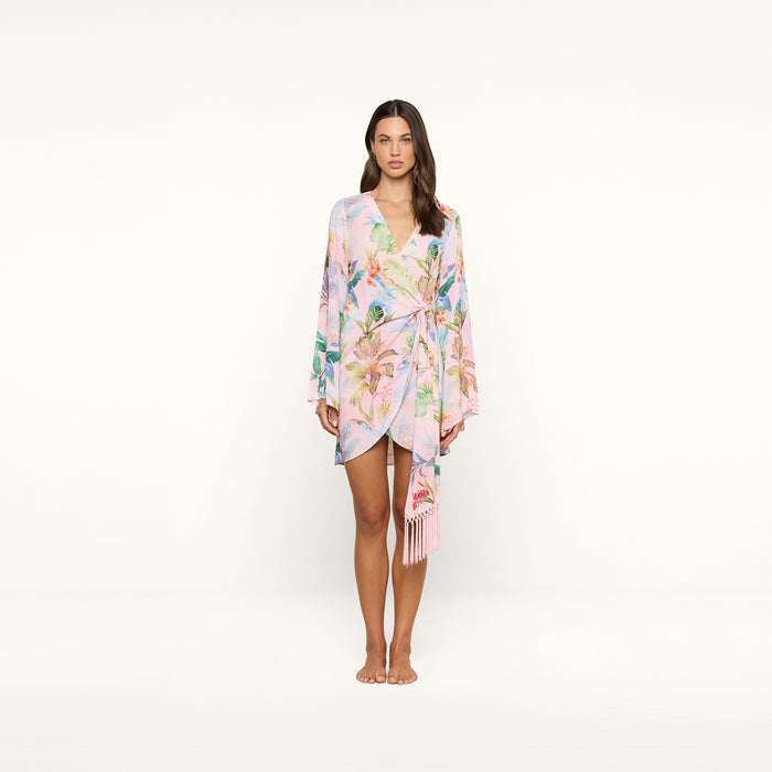 A woman stands facing forward, wearing the Kohima Cover-Up Dress—a pastel floral wrap dress with bell sleeves and a tie at the waist—against a plain white background.