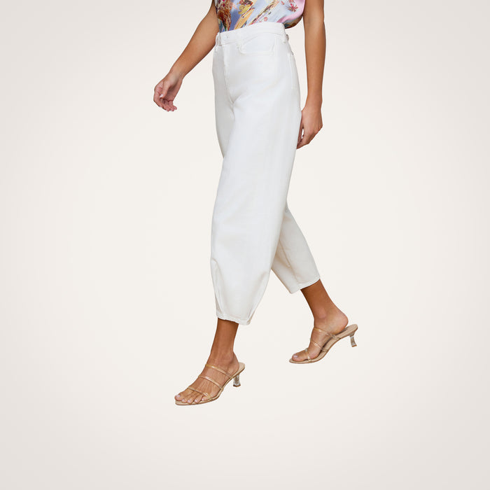 A woman wearing the Krista Tapered Jean in white, a floral sleeveless top, and beige heeled sandals stands against a plain light background. Her face is not visible.