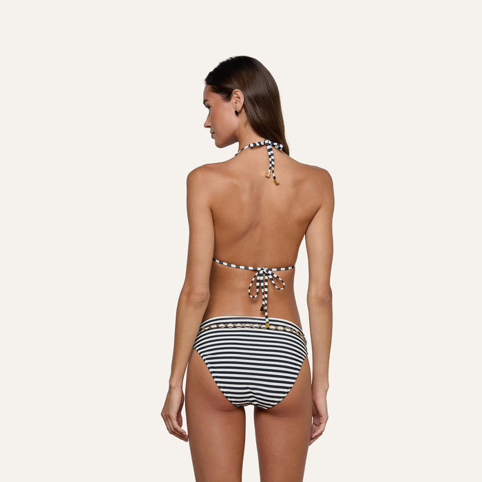 A woman is seen from behind wearing the Kristin Triangle Bikini Top, a black and white striped swimsuit with a halter neck and tie-back design reminiscent of classic French Riviera swimwear, against a plain light background.