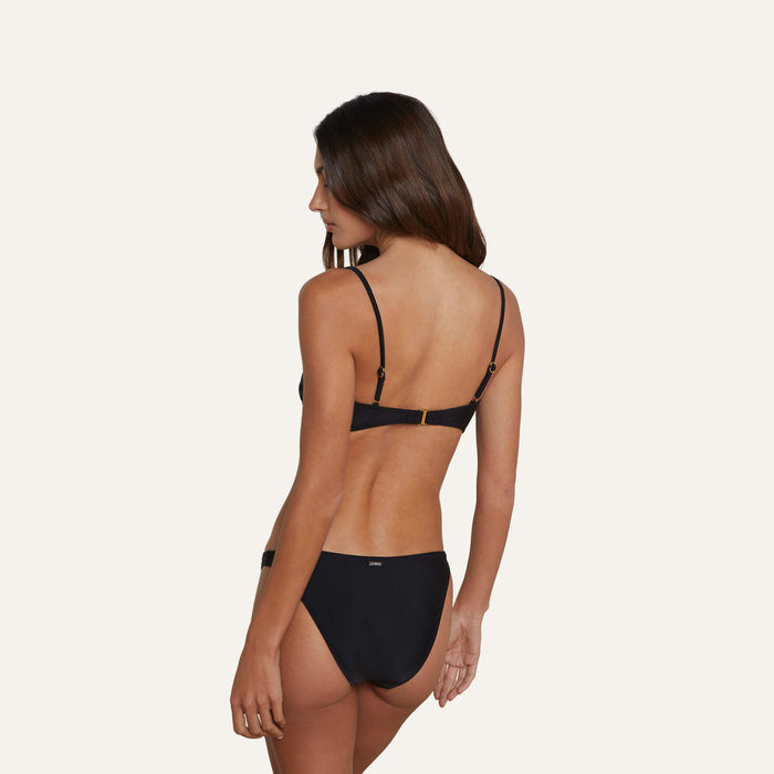 A woman with long brown hair is standing with her back to the camera, wearing the Krysta Bandeau Top against a plain light background.