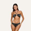Model wearing the Krysta Halter Bikini Top in dark gray, accented with gold ring details and a subtle halter silhouette, standing against a plain light background and looking at the camera.