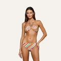 A woman wears the Krysta Halter Bikini Top, featuring colorful stripes and a circular ring detail at the neckline, as she stands against a plain off-white background with one hand on her hip.