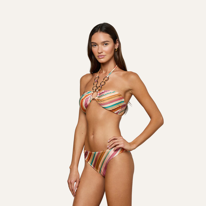 Model wearing the Krysta Halter Bikini Top—a colorful, striped bandeau design featuring a decorative ring and adjustable halter strap—stands against a plain light background. This retro-inspired swimwear look is both playful and stylish.