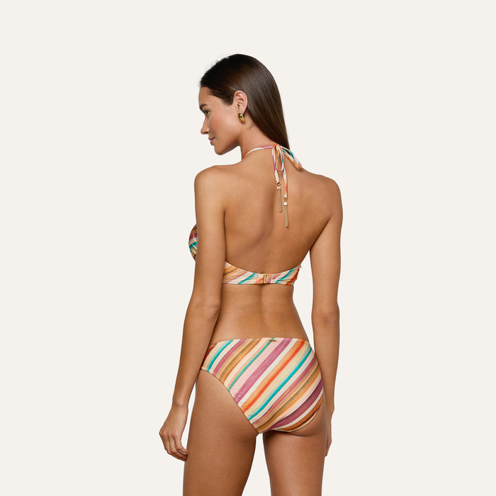 Woman wearing the Krysta Halter Bikini Top, featuring colorful stripes, stands facing away from the camera and looks over her shoulder against a light background.