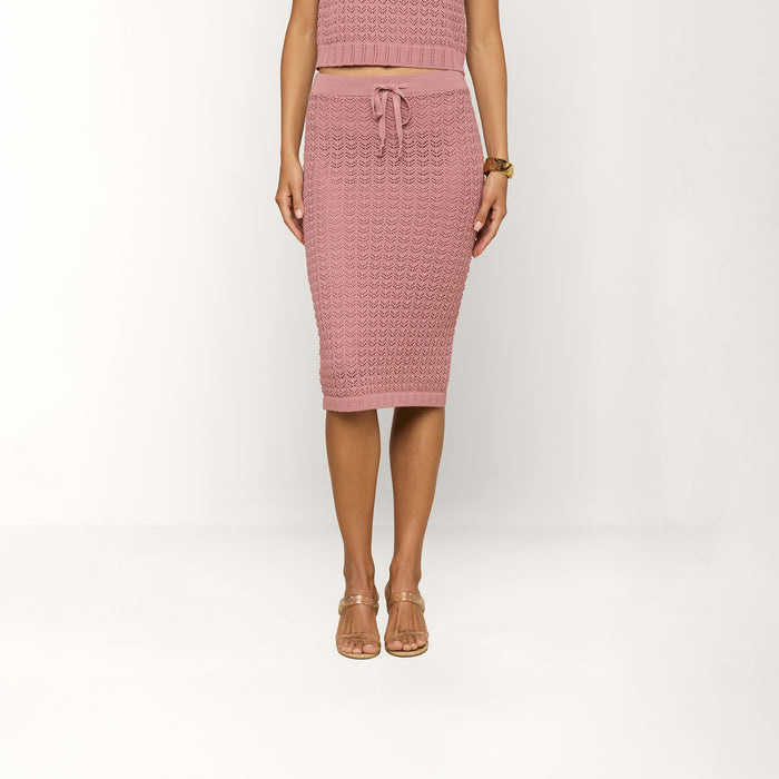 A person wearing the Lacen Pointelle Knit Skirt, a pink breathable knit skirt with a drawstring waist, paired with a matching top, stands barefoot in clear sandals against a white background.