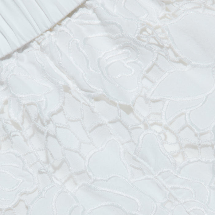 Close-up of the Laina Eyelet Short, featuring white cotton eyelet fabric with a delicate floral lace pattern and gathered elastic detailing at the top edge. The textured, lightweight material makes it perfect for warm-weather wear or beach outings.