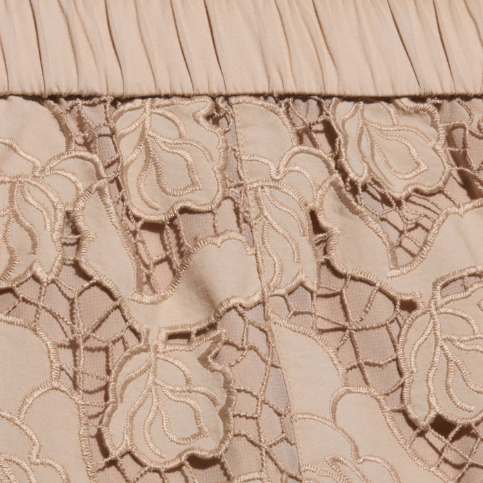 Close-up of almond tan fabric with floral lace embroidery and pleated detailing at the top edge. The lace features intricate flower patterns over a solid background, reminiscent of the delicate design found in the Laina Eyelet Short.