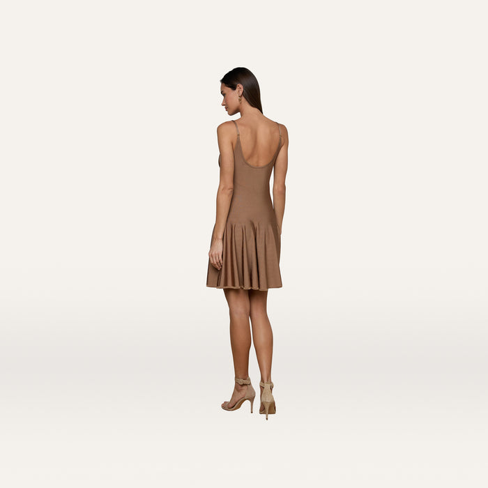 A woman stands facing away against a plain white background, wearing the Lana Knit Dress—a sleeveless brown stretch knit design with a flared skirt—paired with beige high-heeled sandals.
