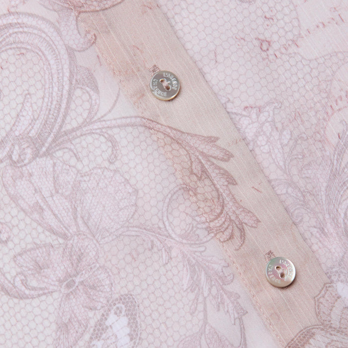 Close-up of the Laurent Blouse in sheer light pink poly chiffon, featuring intricate floral and butterfly patterns, visible stitching, and two metallic buttons along the seam.